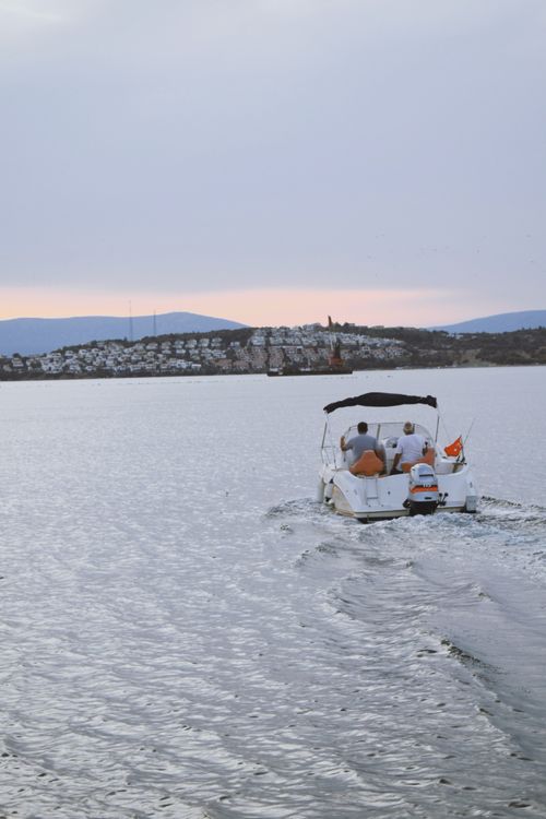 Free A peaceful scene of a motorboat cruising on a bay at sunset with a distant town view. Stock Photo