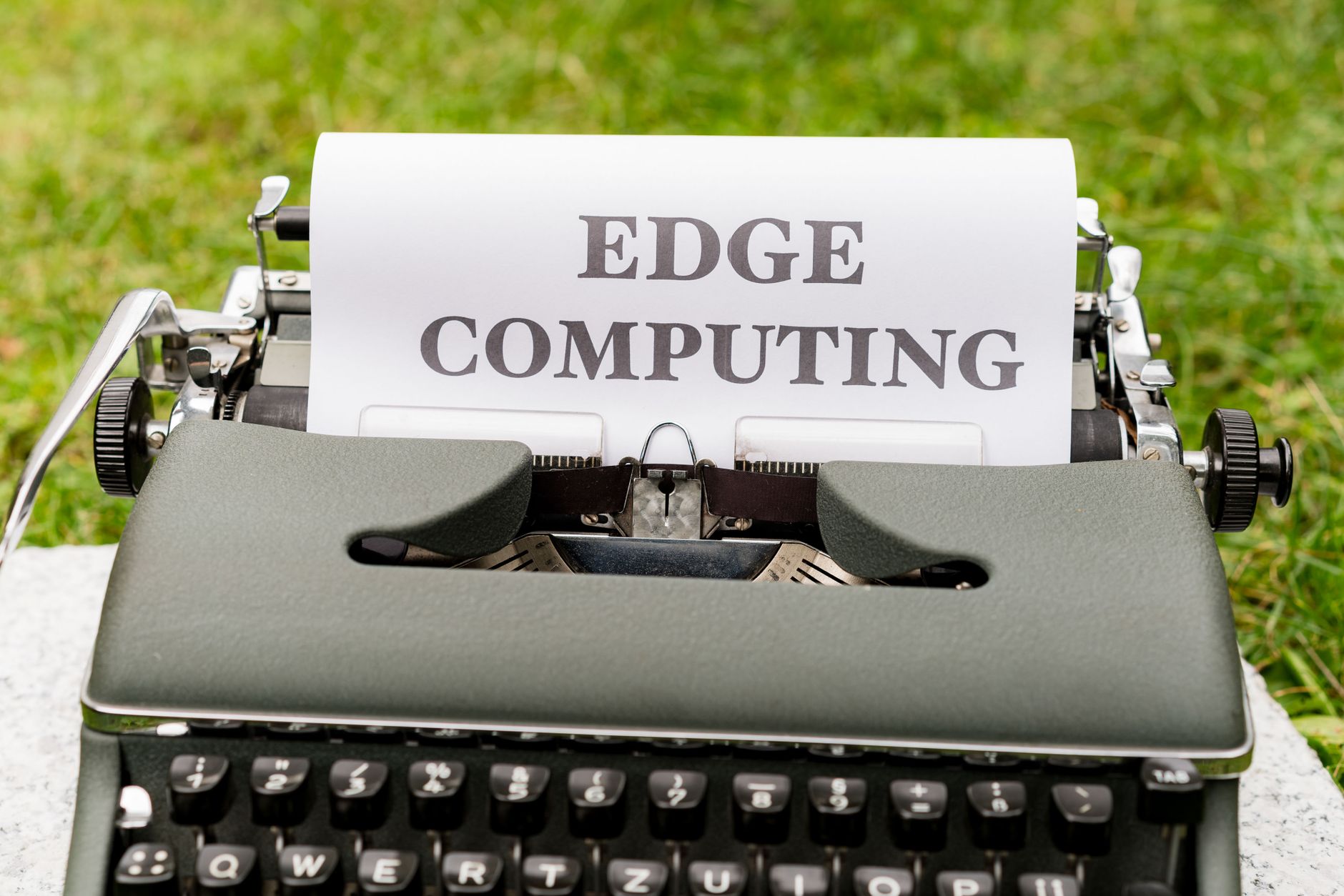 A vintage typewriter outdoors typing 'EDGE COMPUTING' on paper, blending technology with nostalgia.