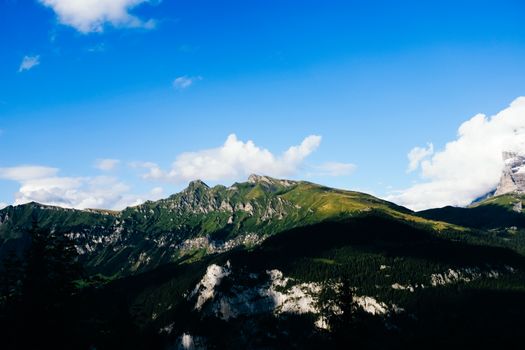Breathtaking view of a green mountainous landscape under a vibrant blue sky with fluffy clouds.