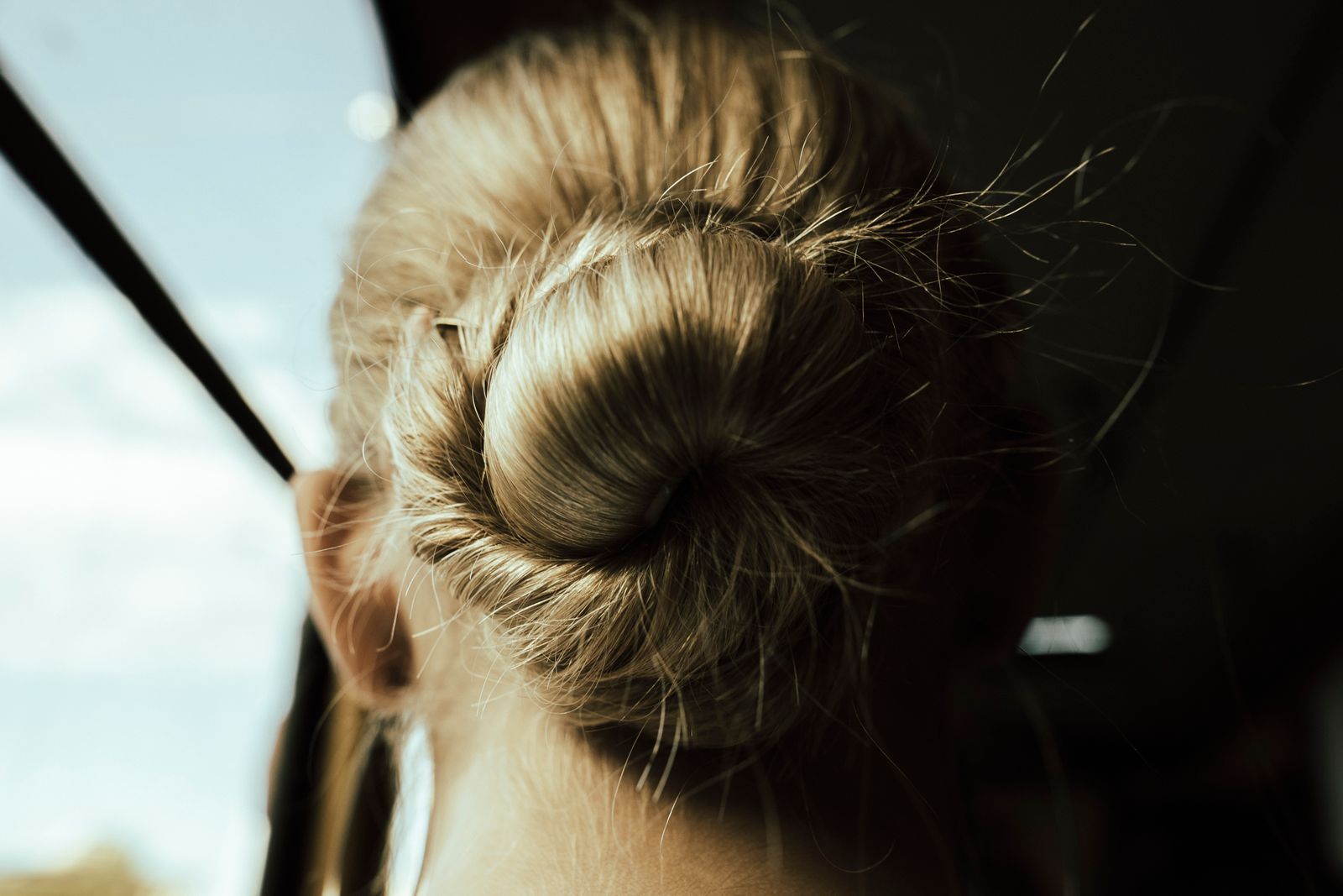 Close-up of the back of a woman's head with a blonde hair bun lit by warm sunlight