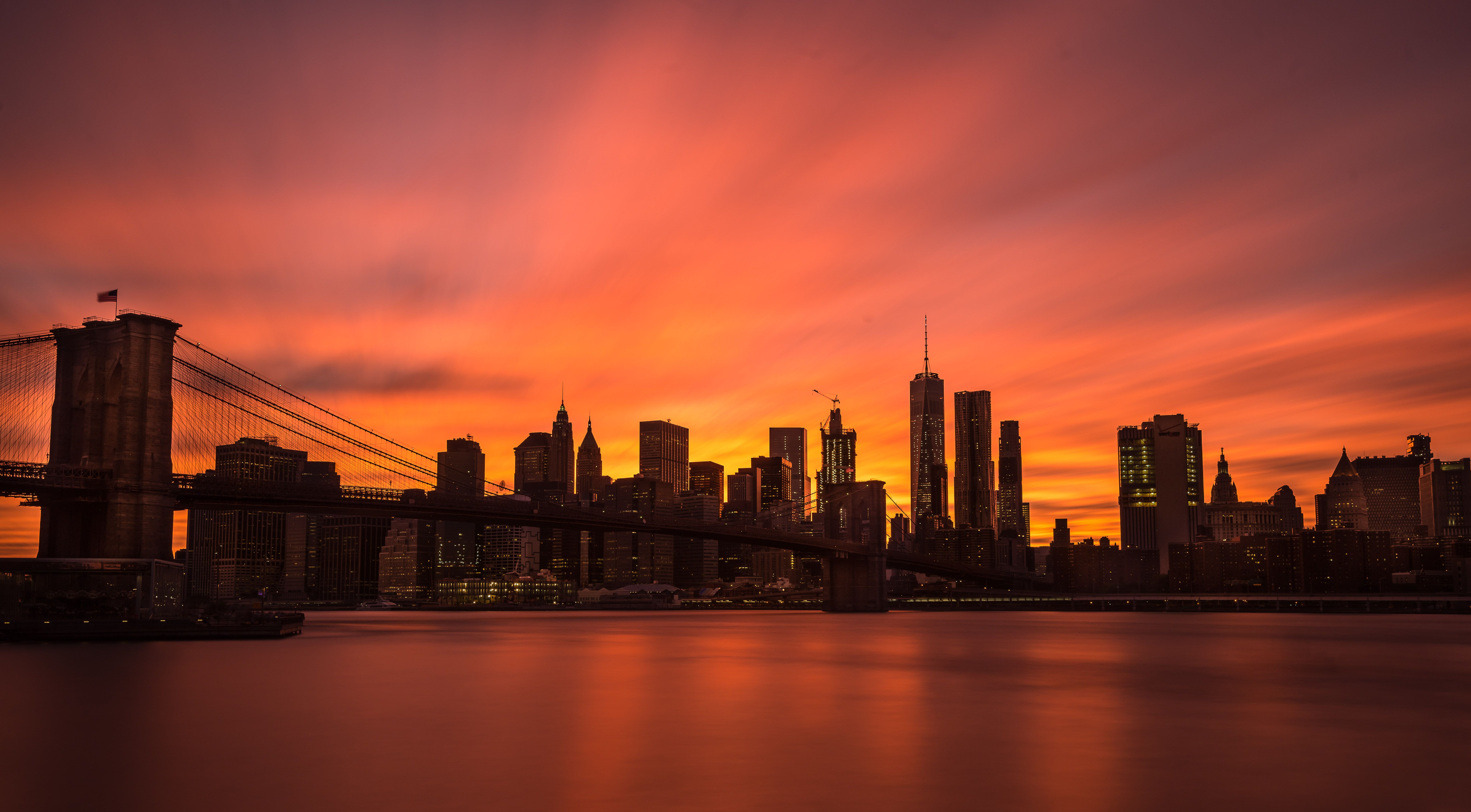 Stunning view of Brooklyn Bridge and Manhattan skyline under a dramatic sunset sky.