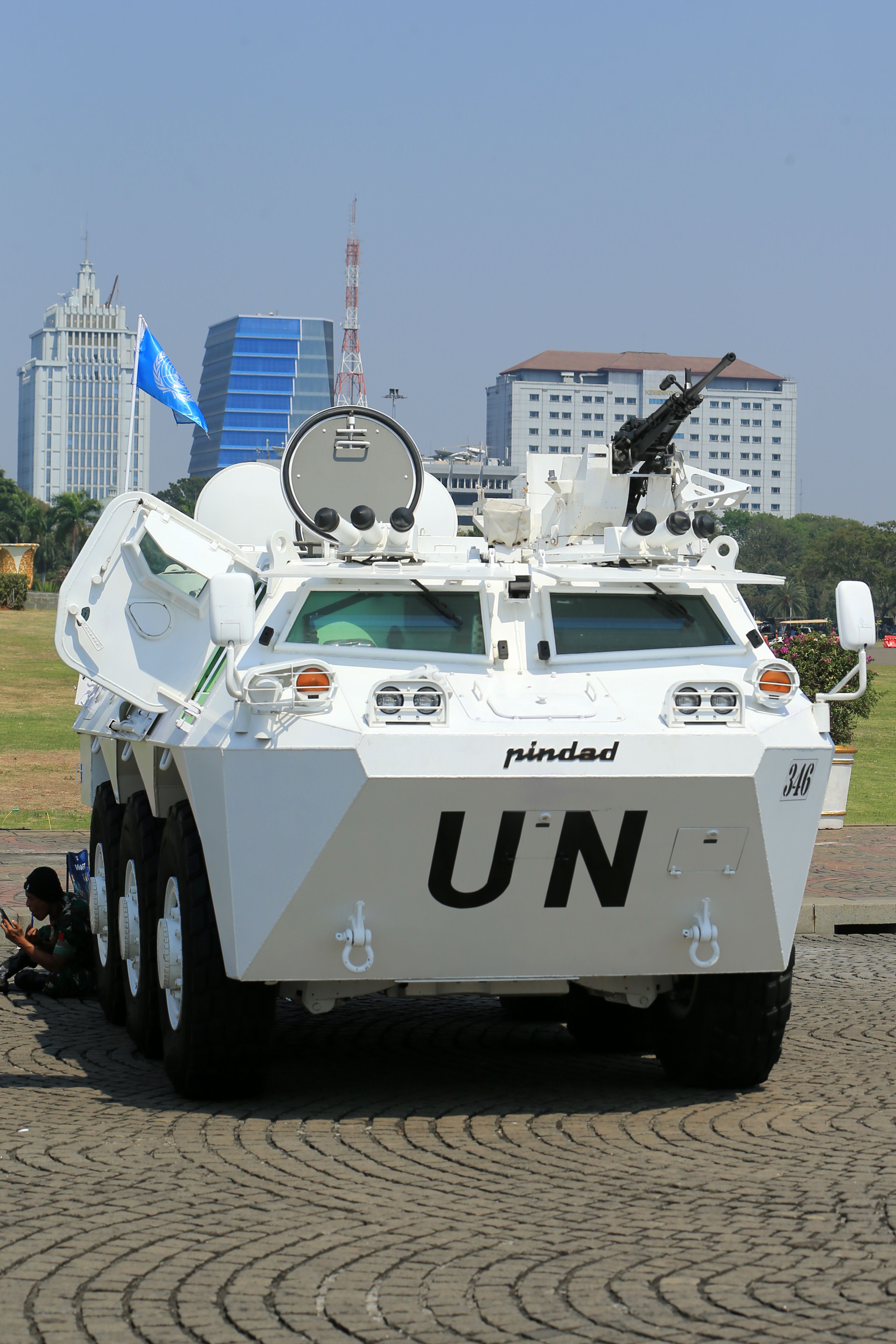 A white UN armored vehicle parked in a city area with buildings in the background.