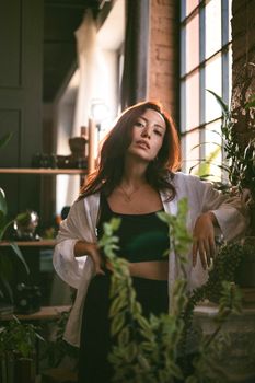 Stylish woman in a sunlit room surrounded by lush greenery, exuding elegance and calm.