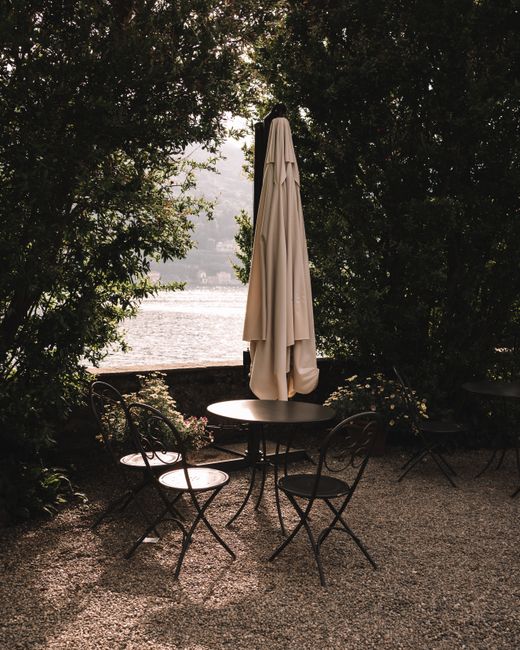 Serene lakeside terrace in Stresa, Italy with chairs and umbrella, framed by greenery.