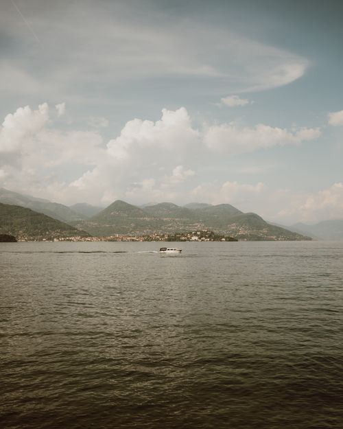 Free A serene view of a motorboat on Lake Maggiore, Italy with distant hills and clouds. Stock Photo