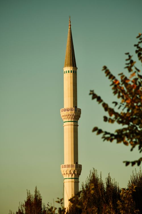 Free A tall minaret against a sunset sky framed by tree branches, exuding a serene evening ambiance. Stock Photo