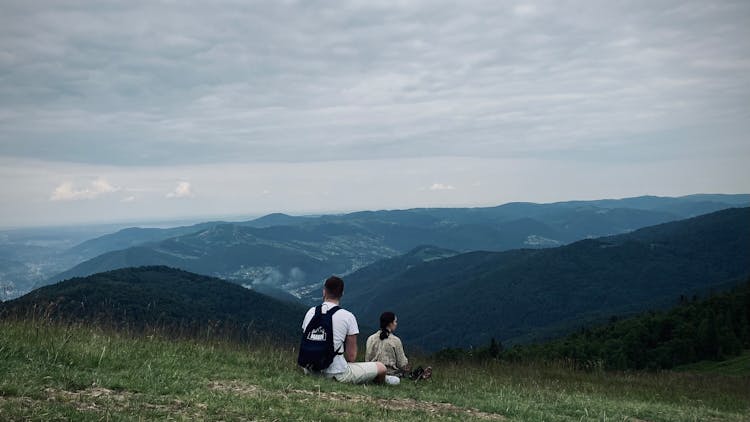 A Man And Woman Sitting On The Ground In Mountains