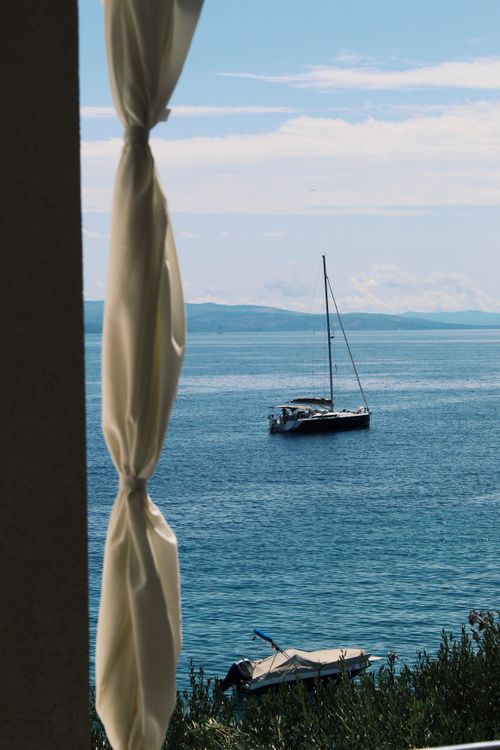 Free Tranquil seaside scene with a sailboat viewed through a curtain on a sunny day. Stock Photo