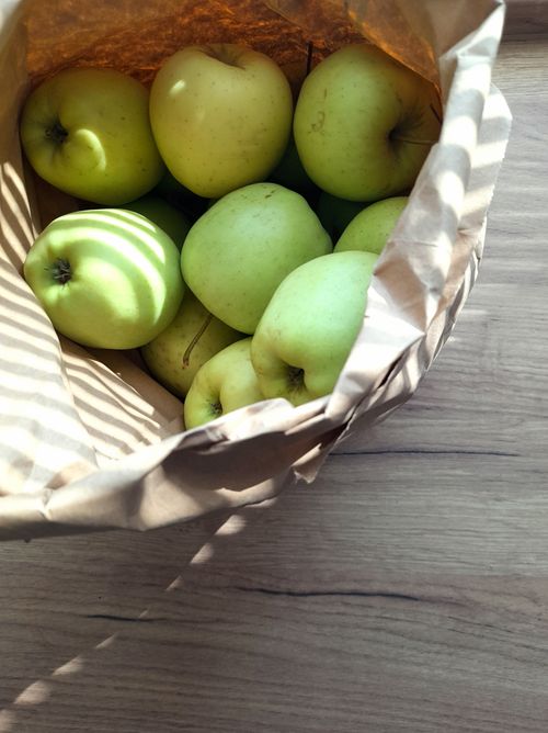 Free Top view of green apples in a paper bag on a wooden table, bathed in sunlight. Stock Photo