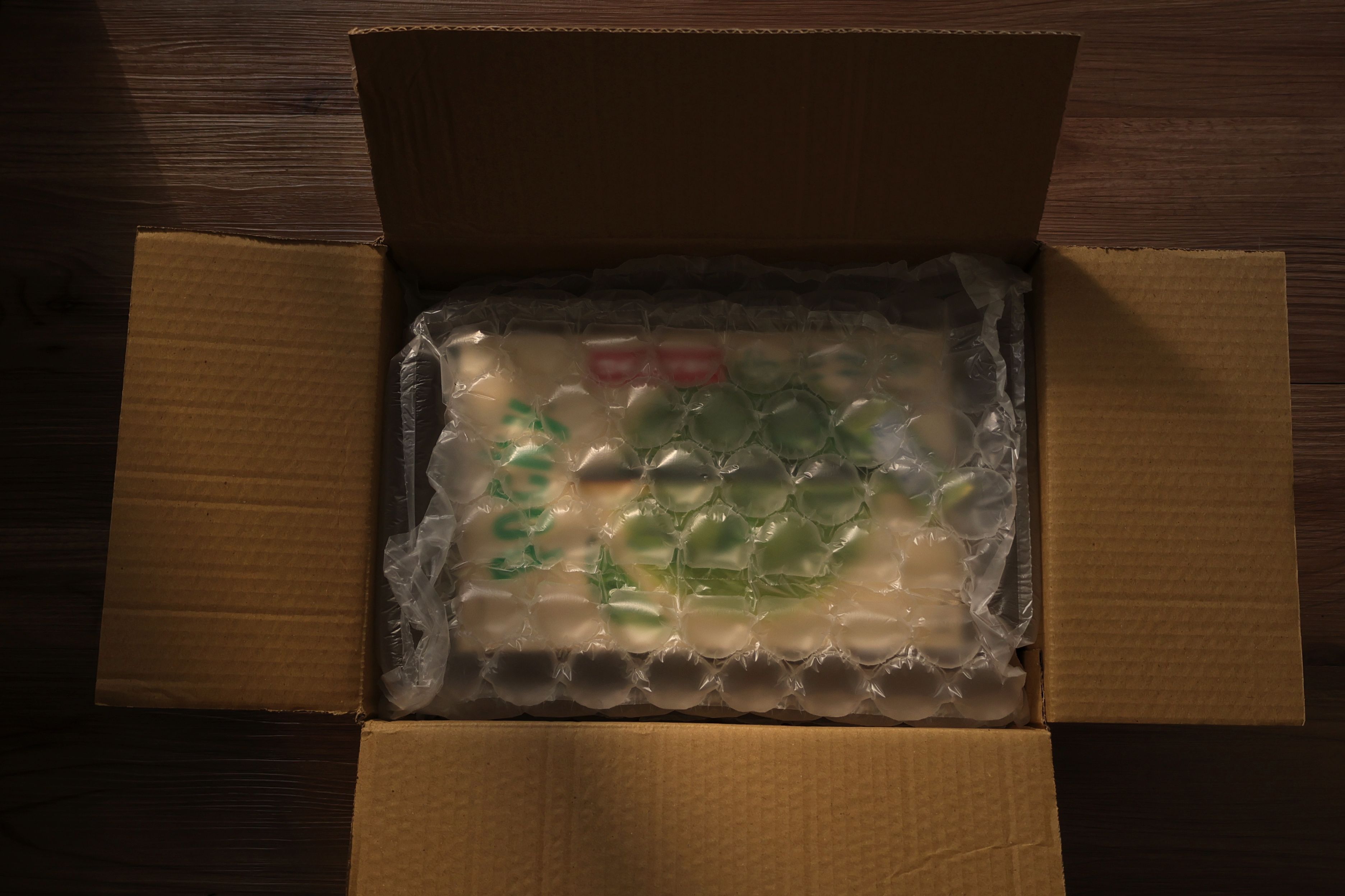 Open cardboard box displaying bubble-wrapped content, photographed indoors with soft lighting.
