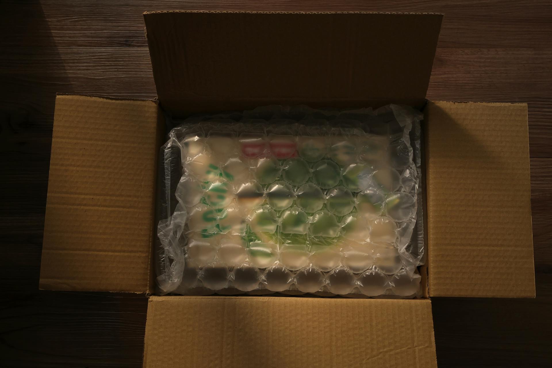 Open cardboard box displaying bubble-wrapped content, photographed indoors with soft lighting.