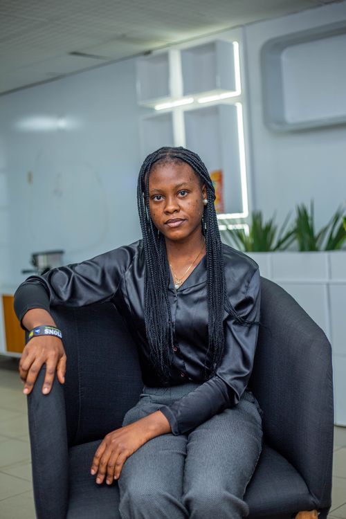 Free Stylish African woman in a sleek black shirt seated indoors, showcasing modern interior design. Stock Photo