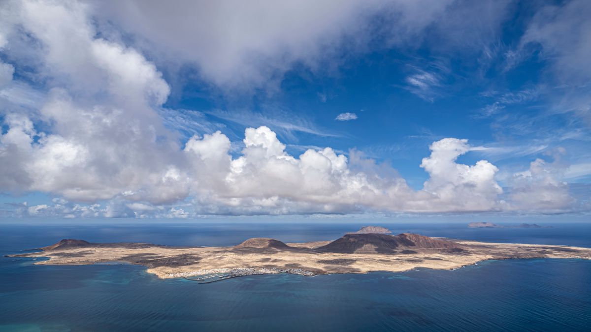 Insula La Graciosa văzută de sus de la Mirador del Río, cu oceanul și un cer cu nori