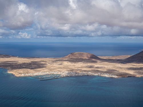 Free Breathtaking aerial view of an island coast surrounded by blue ocean and dramatic clouds. Stock Photo
