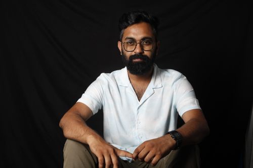 Free Bearded man with glasses in a white shirt posing against a black studio backdrop. Stock Photo