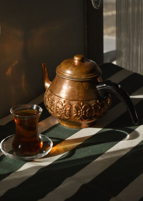 Free Warm sunlight over copper teapot and Turkish tea glass on striped tablecloth indoors. Stock Photo
