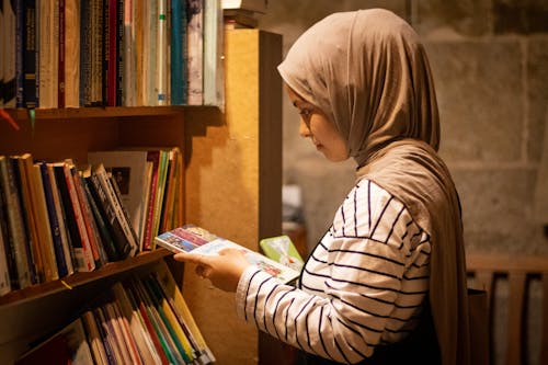 Side View of a Young Woman in a Hijab Holding a Book in a Library 