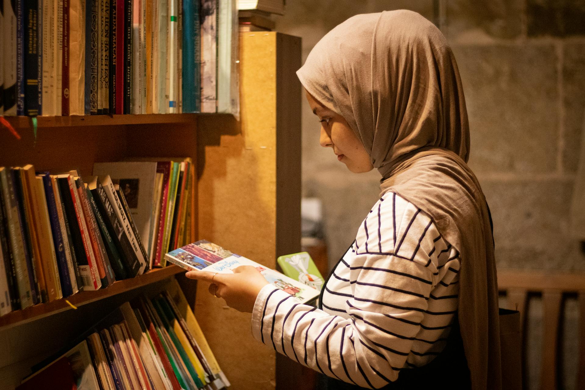 A young woman wearing a hijab reading a book in a library in Kayseri, Türkiye.