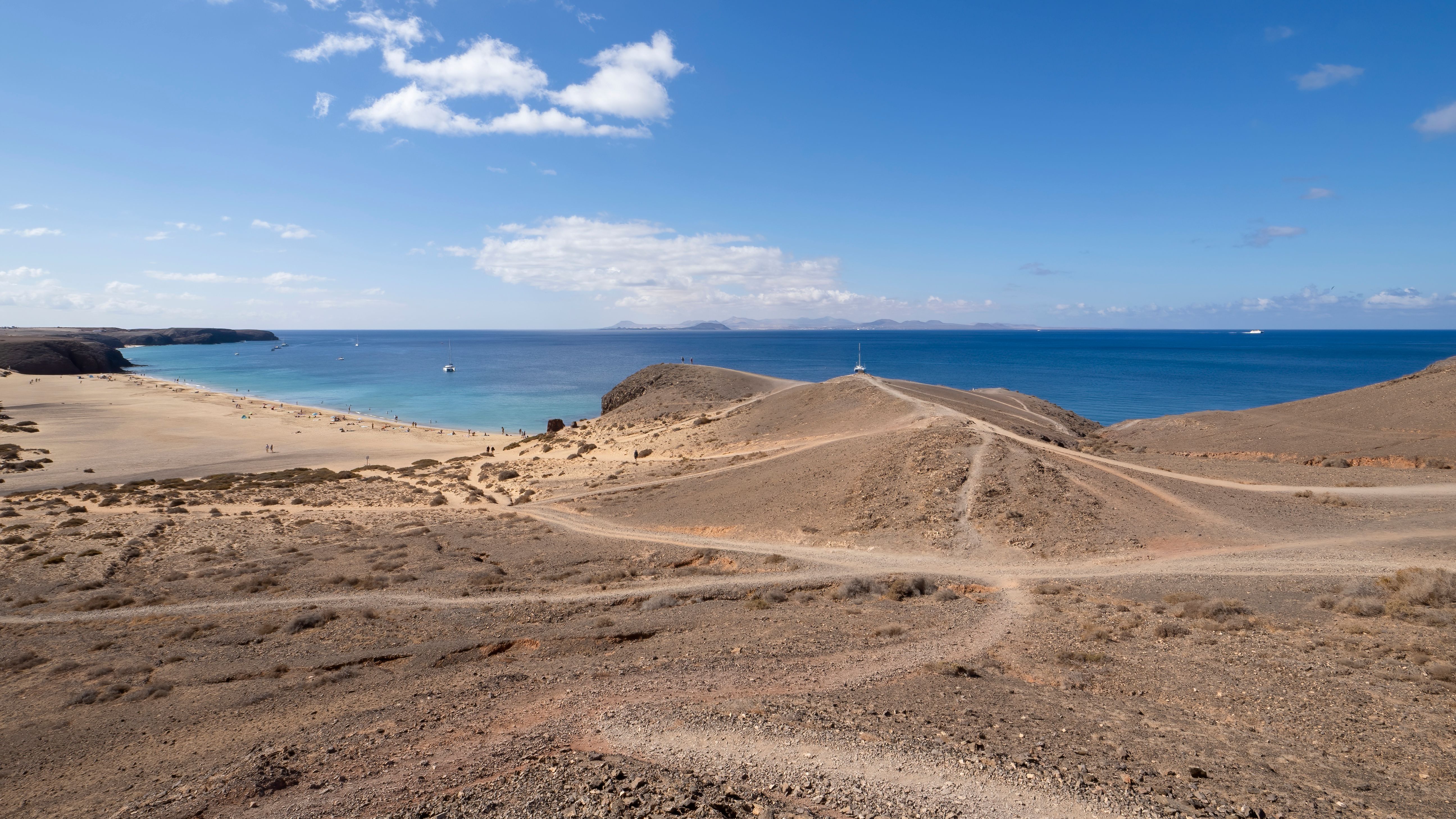 Stunning coastline view of Lanzarote featuring sandy beaches, barren landscape, and clear blue sea under a bright sky.