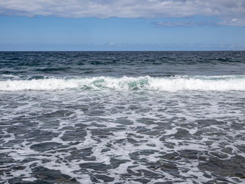 Free Tranquil ocean scene with gentle waves rolling onto the shore under a clear blue sky. Stock Photo