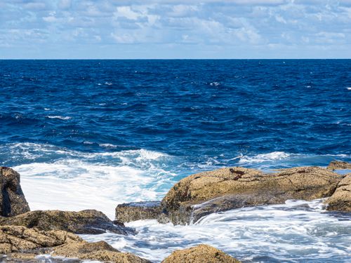 Free Vivid scene of waves crashing on a rocky coastline under a bright blue sky. Stock Photo