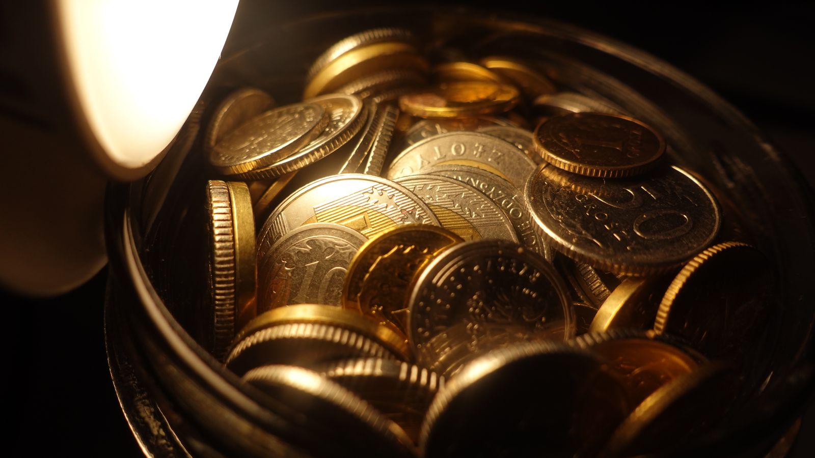 Assorted coins gathered in a glass jar under warm light