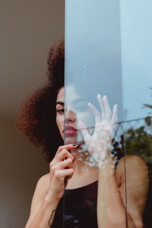 Free Artistic portrait of a woman with natural afro hair behind a glass pane, offering a modern touch. Stock Photo