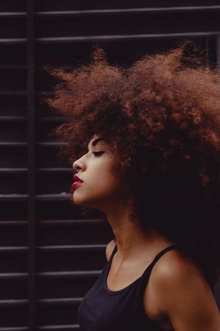 Striking portrait of a woman with afro hairstyle and bright lipstick, showcasing elegance and style.