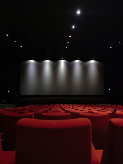 An empty cinema with red seats facing a dark screen