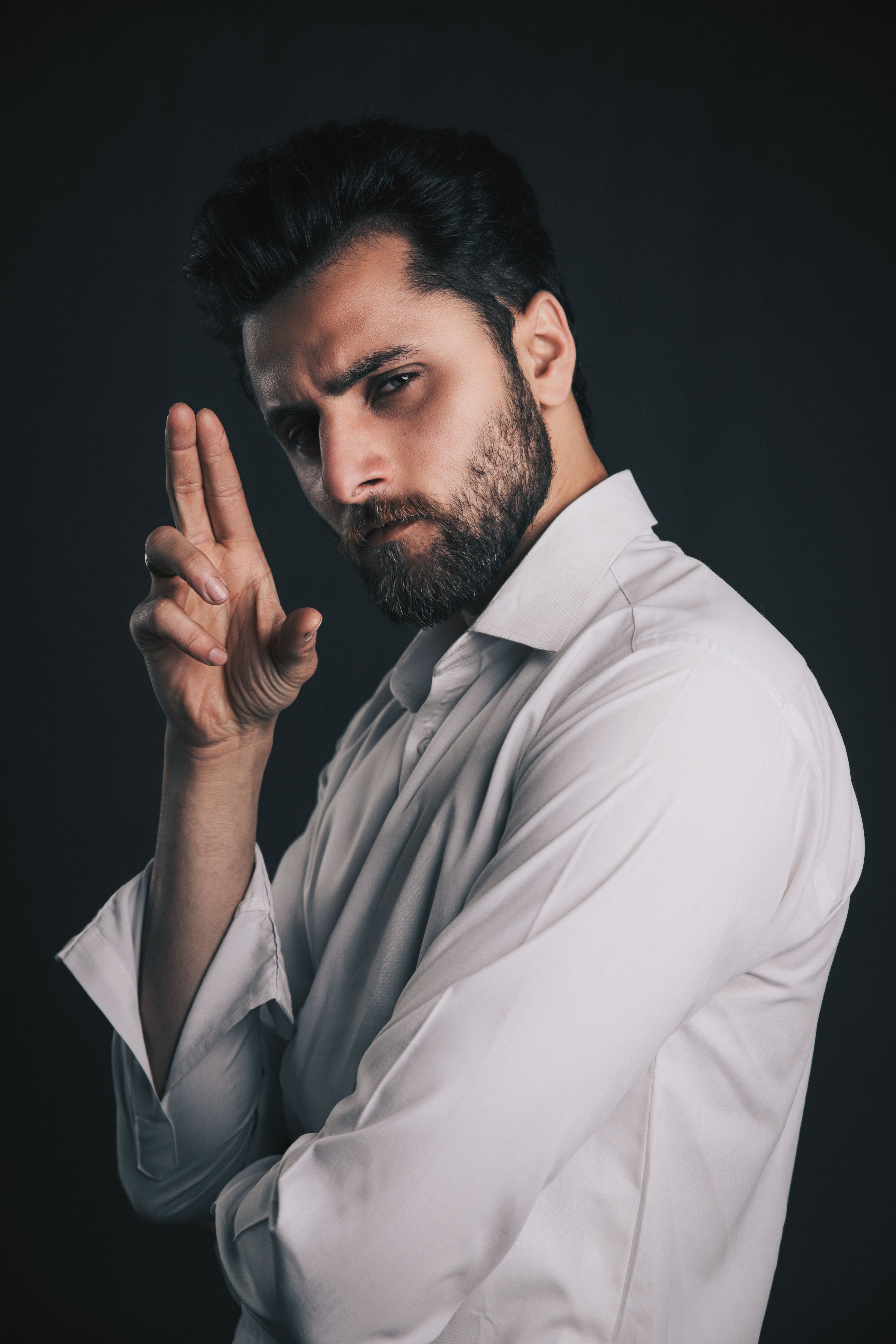 A confident man with a beard poses stylishly in a studio wearing a white shirt.