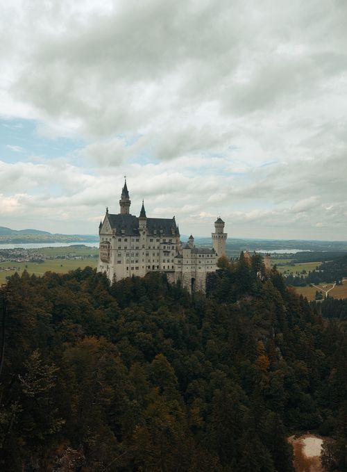 Free Majestic Neuschwanstein Castle atop a forested hill under cloudy skies in Bavaria, Germany. Stock Photo