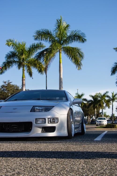 Free A sleek silver sports car parked in a lot surrounded by palm trees on a bright sunny day. Stock Photo