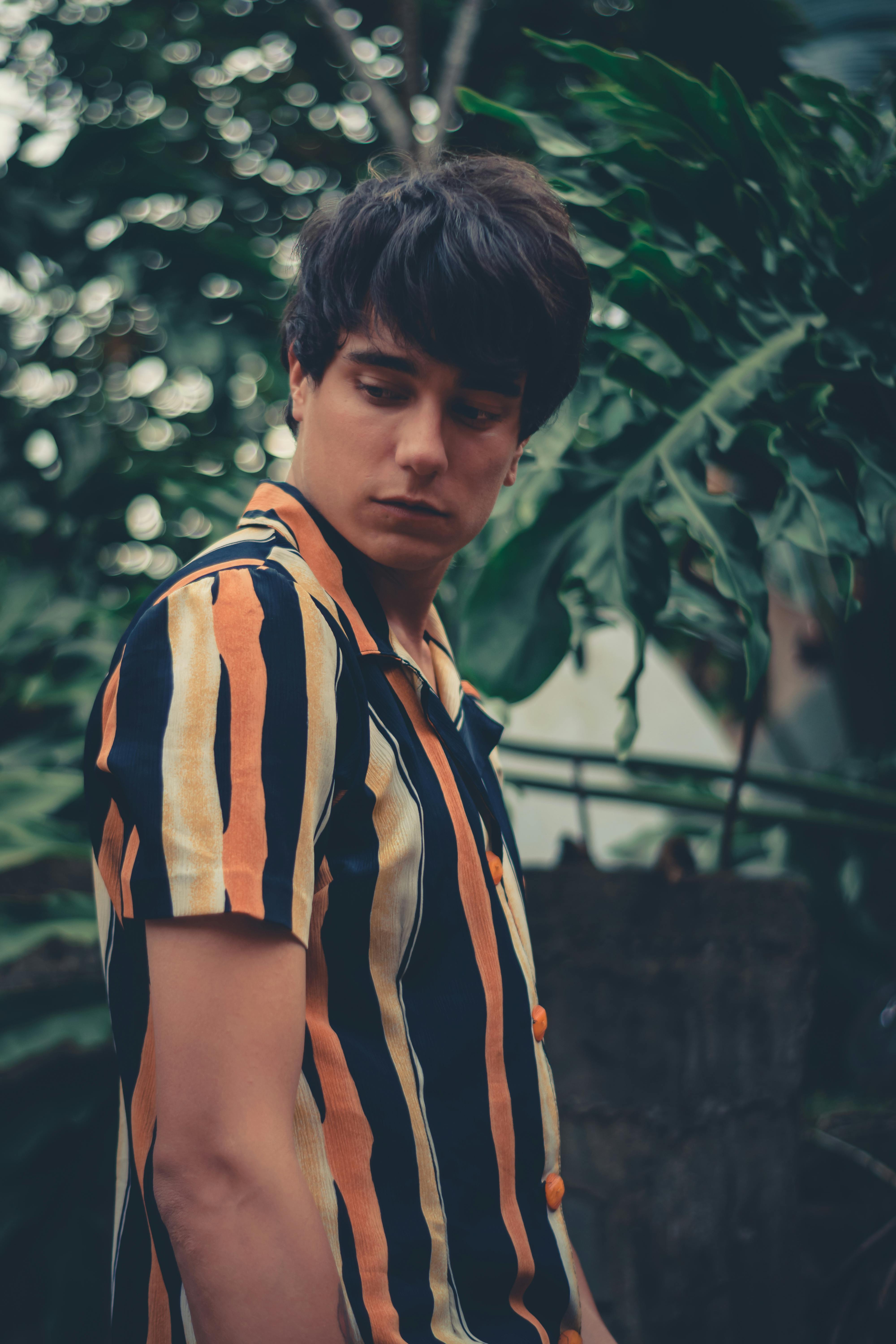 一位穿着条纹衬衫的年轻人在郁郁葱葱的绿色植物前摆姿势