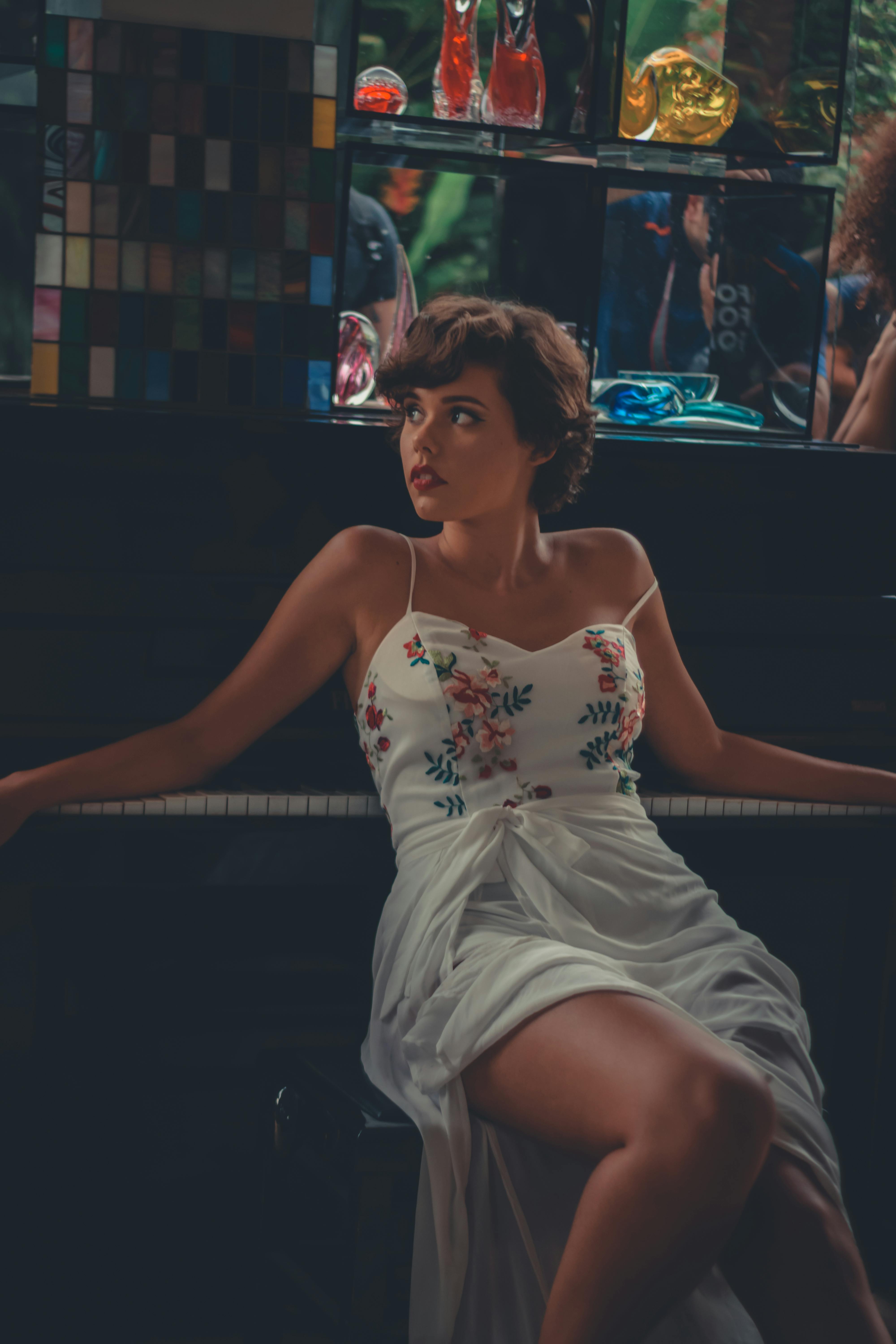 woman wearing white and multicolored floral spaghetti strap dress sitting on chair beside piano
