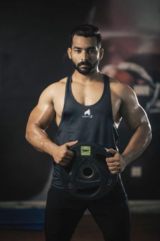 Muscular man in sportswear holding weight plate in a gym. Fitness and strength training concept.