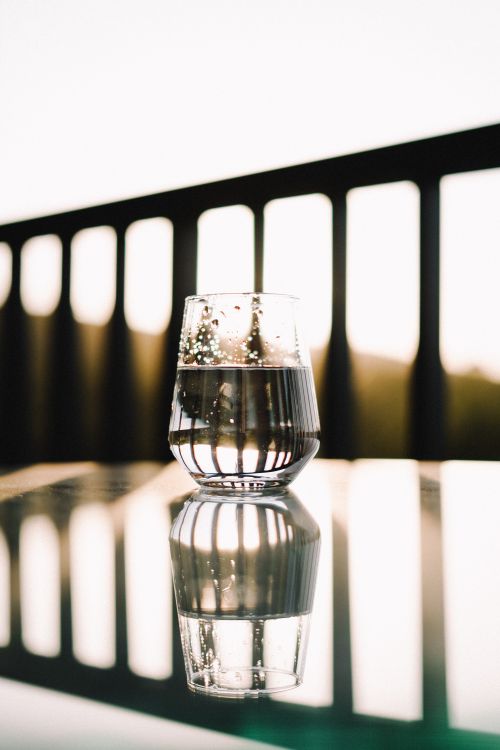 Free A glass of water reflects the warm glow of the sunset on a balcony, creating a captivating visual. Stock Photo