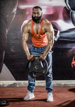 Bearded bodybuilder in tank top lifting heavy weight indoors, showcasing strength and fitness.