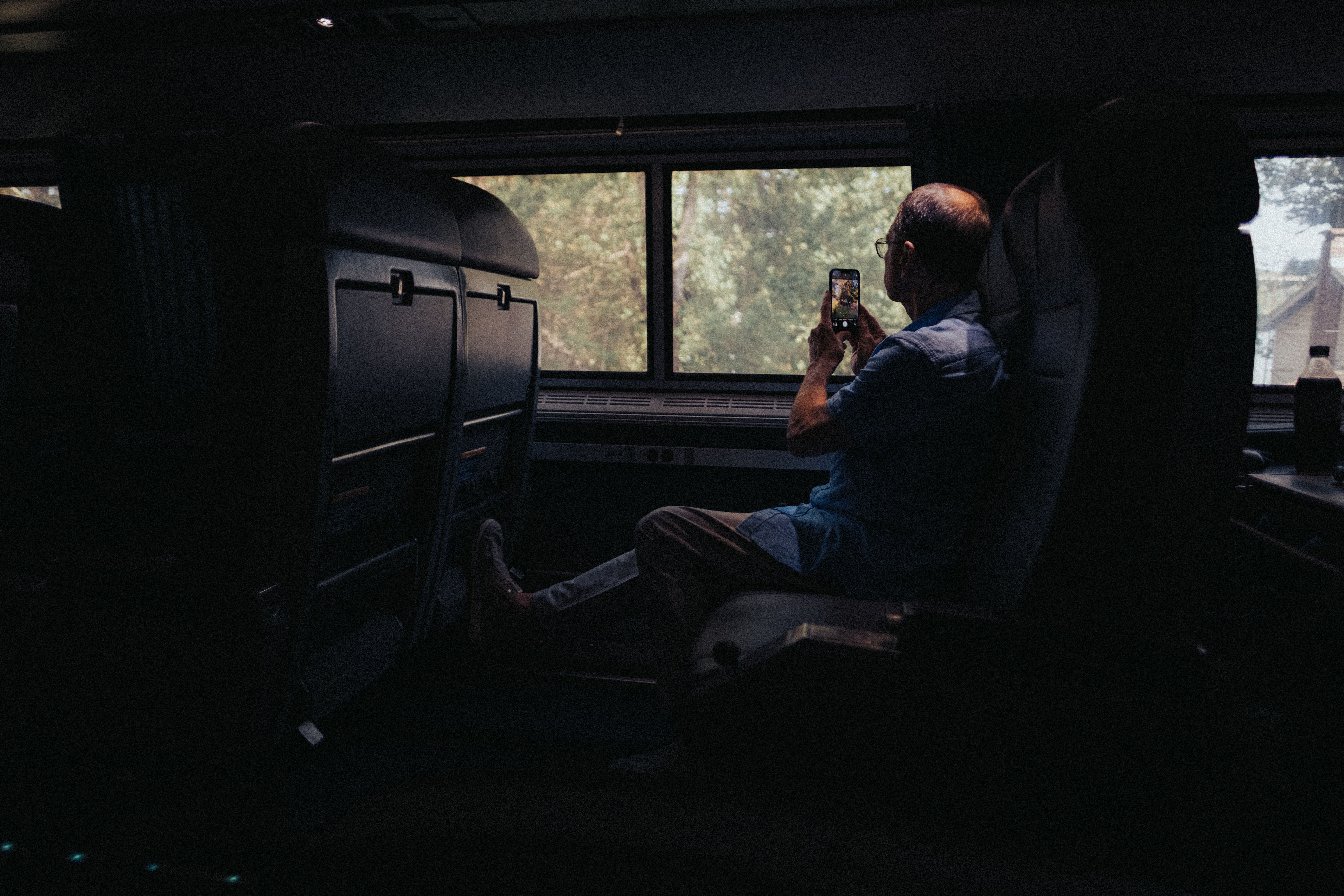 Senior man captures scenic views from a train window using a smartphone.