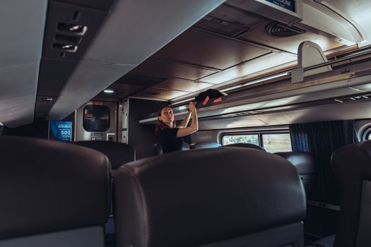 Female traveler stowing luggage in a train overhead compartment, emphasizing modern passenger travel.