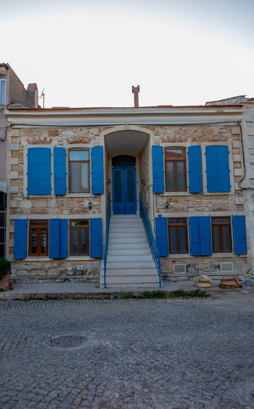 Free Stone house with vibrant blue shutters and stairs located outdoors in Foça, İzmir, Türkiye. Stock Photo