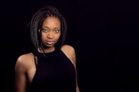 一位自信的黑人女性肖像令人惊叹，她梳着辫子，在深色背景下熠熠生辉