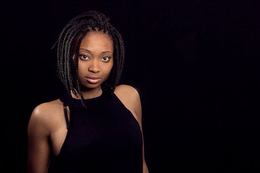 一位自信的黑人女性肖像令人惊叹，她梳着辫子，在深色背景下熠熠生辉