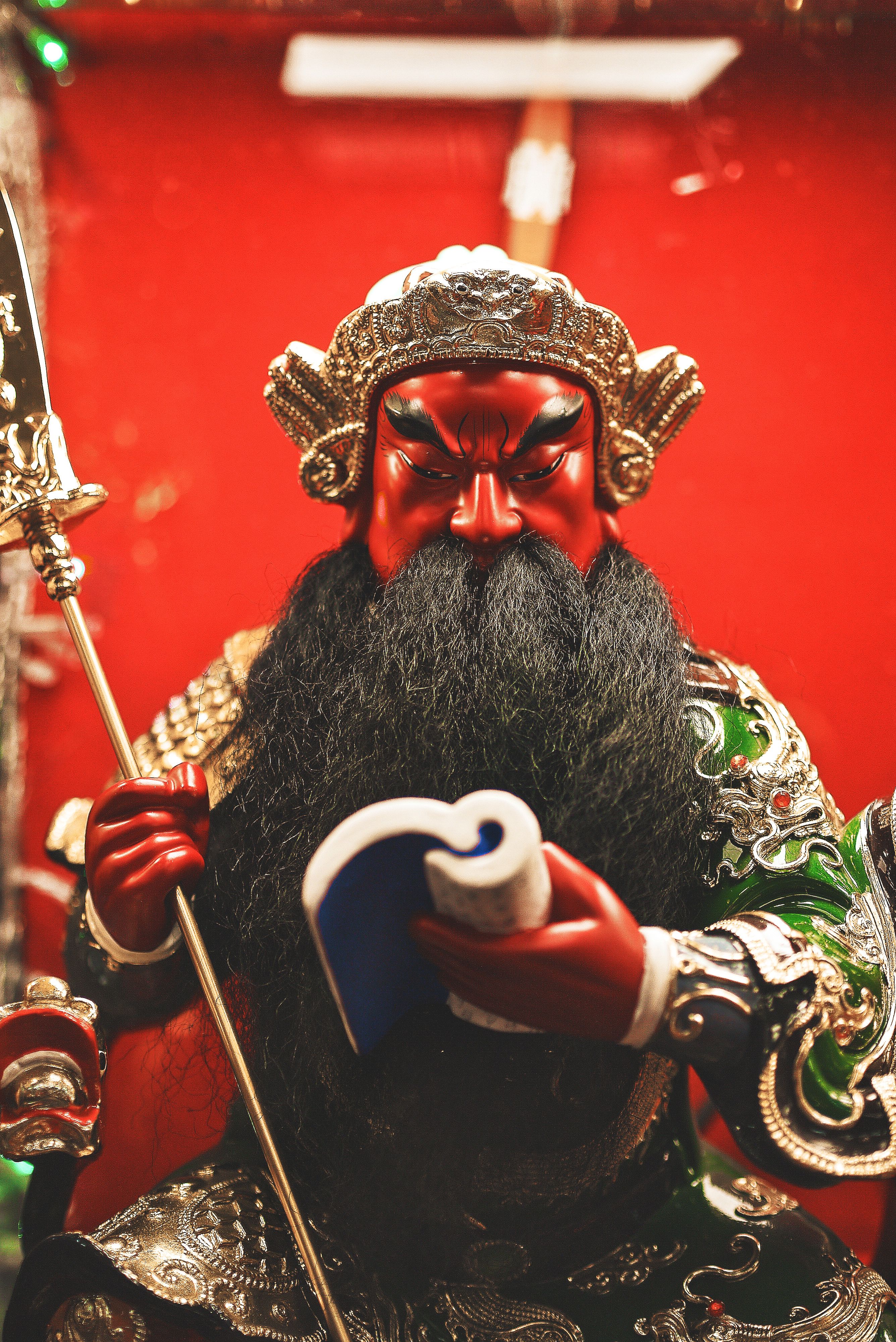 Detailed statue of a warrior with red face and black beard, holding a book.