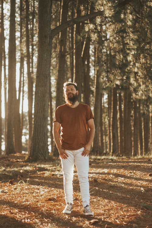 Bearded Man Wearing a T-Shirt and White Pants Standing in a Forest