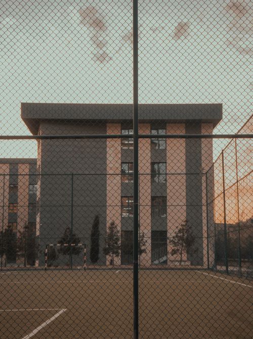 Free Exterior view of a modern school building with a fenced soccer field at dusk. Stock Photo