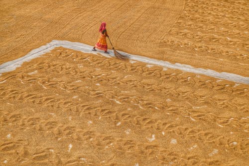 Aerial View of a Woman Walking on a Field with a Broom 