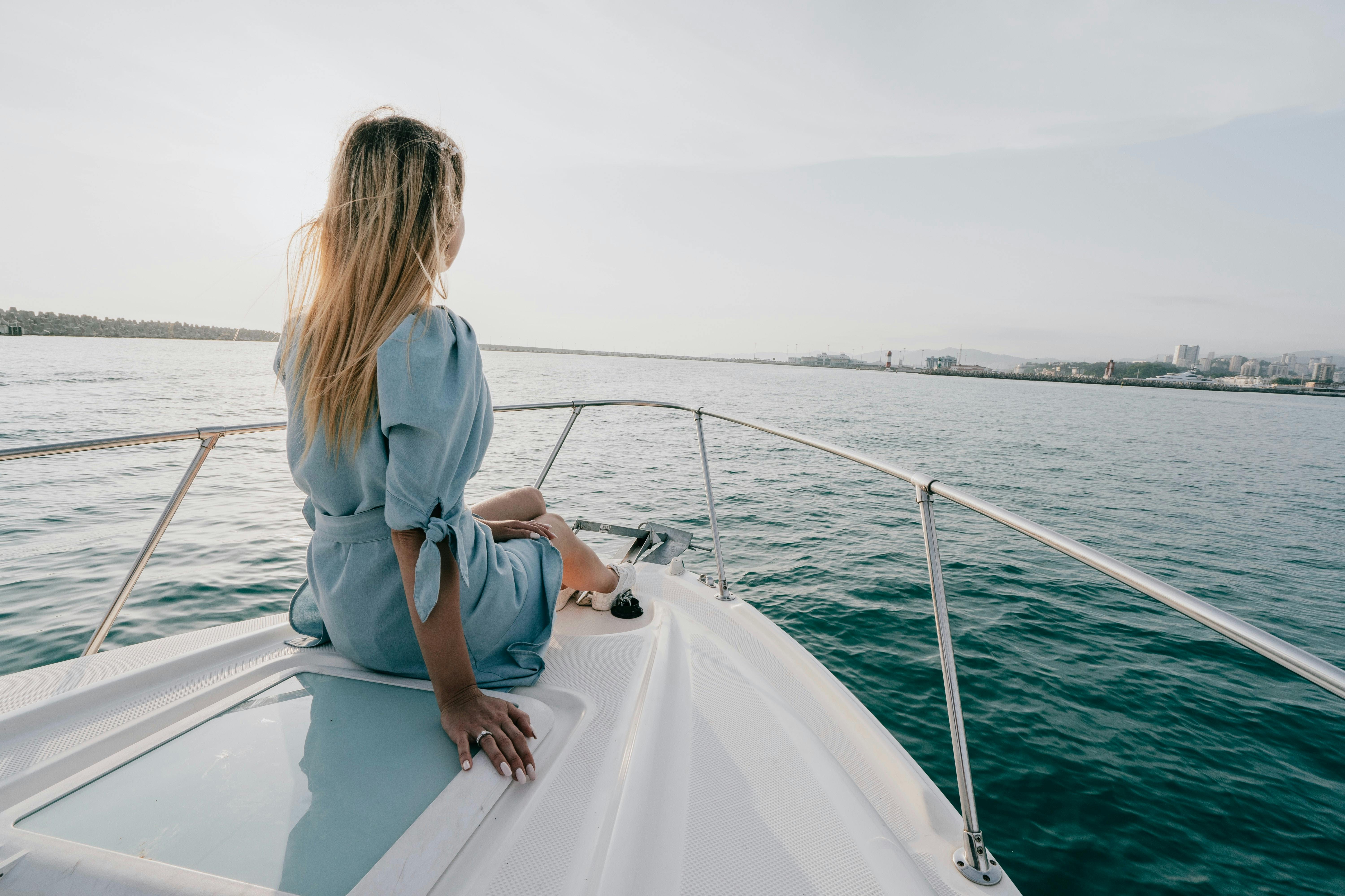 A woman in a blue dress enjoys a peaceful moment on a yacht's deck, overlooking the vast sea.