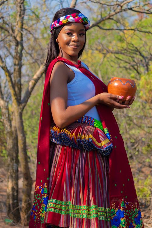 Free Portrait of a smiling woman in traditional African attire holding a clay pot outdoors. Stock Photo