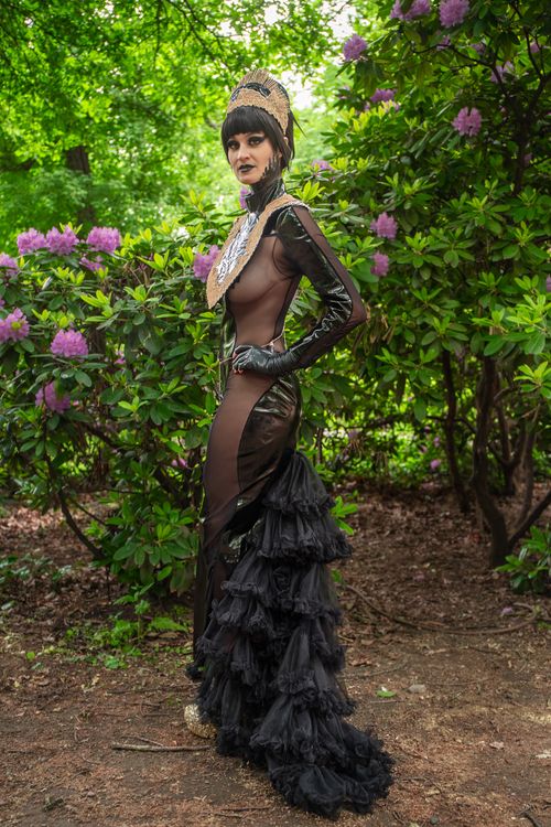 Free A model in a chic black gown poses amidst lush greenery and vibrant flowers, showcasing elegance and style. Stock Photo