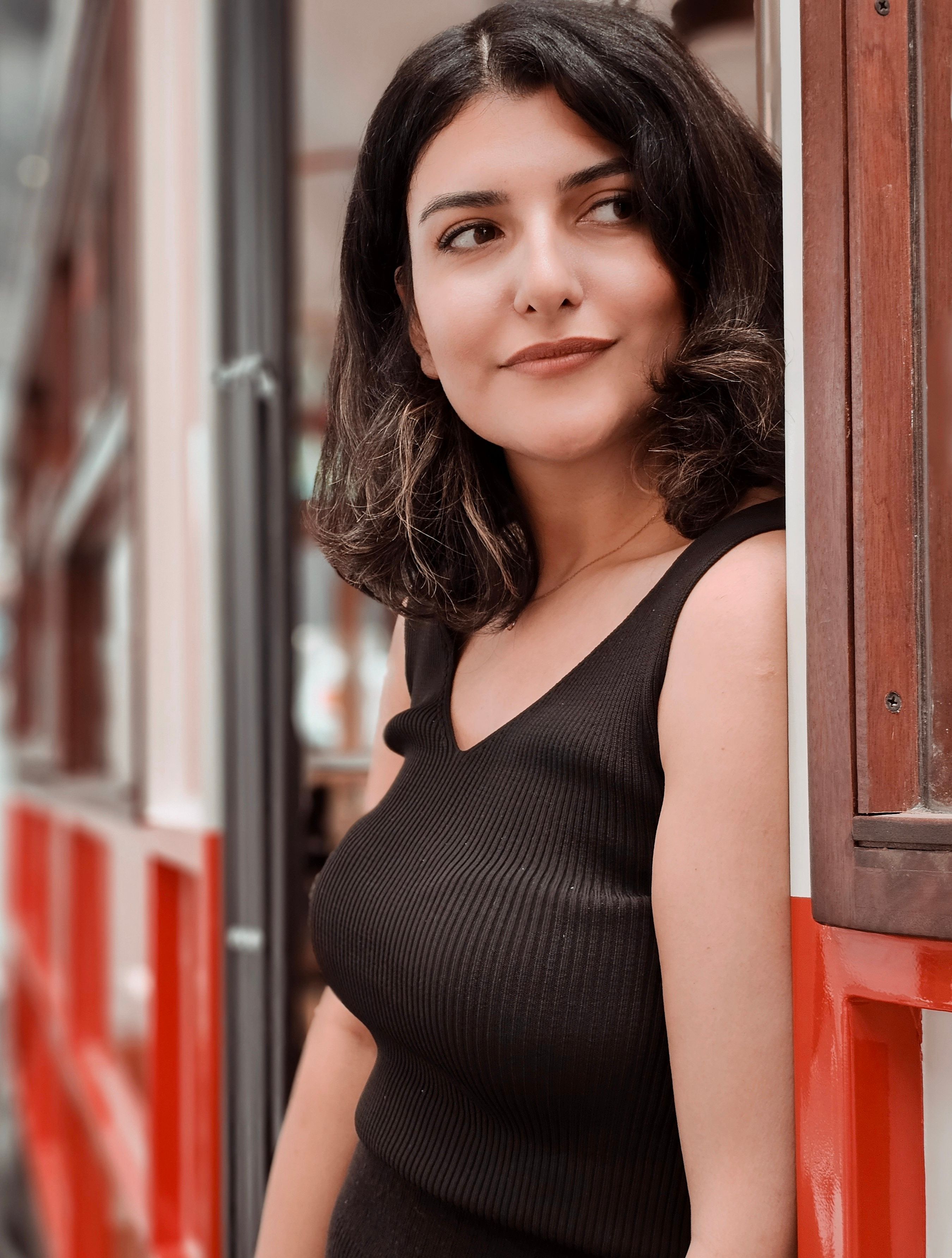 Portrait of a smiling woman standing by a red tram entrance.